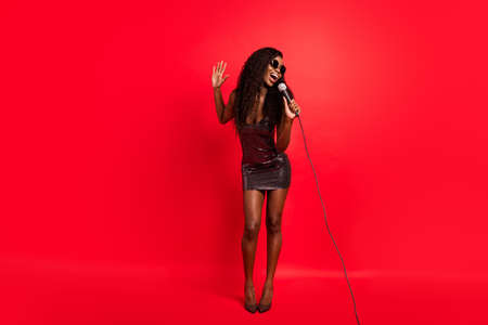 Full size photo of young african woman sing pop song microphone performance stage isolated over red color backgroundの写真素材