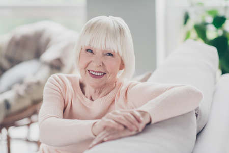 Photo portrait smiling granny sitting on soft sofa in warm sweater staying at home during lockdownの写真素材