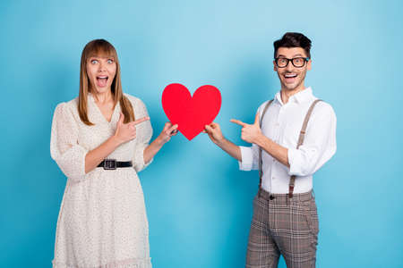 Photo of funny excited two persons dressed white clothes holding pointing fingers big paper heart...