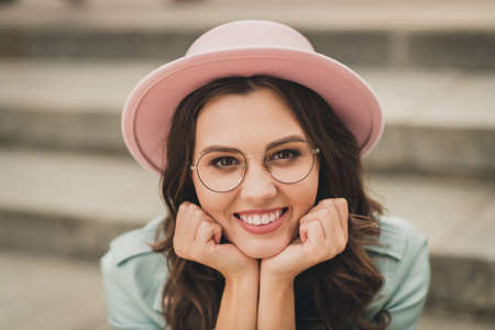 Photo of dreamy thoughtful young woman dressed teal jacket glasses sitting stairs arms chin outdoors urban cityの写真素材