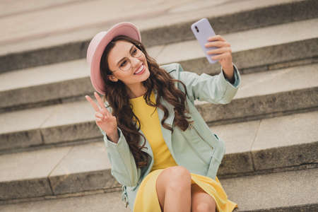 Portrait of attractive girl sit on stair make selfie fingers show v-sign have good mood free time...