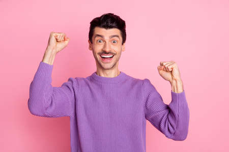 Photo of lucky cute young man dressed purple pullover rising fists isolated pink color backgroundの写真素材