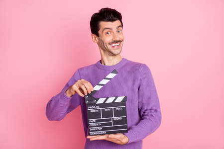 Photo of funny sweet young man dressed purple pullover holding clapperboard isolated pink color backgroundの写真素材