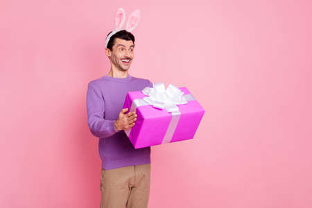Photo of funky excited young man dressed purple pullover hare ears gift box looking empty space...
