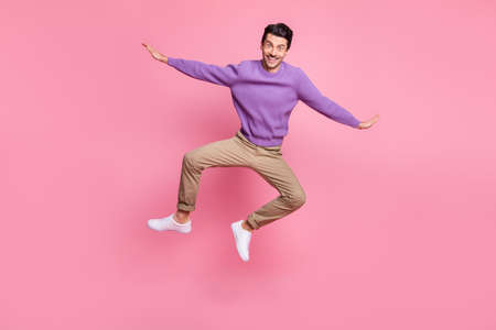 Photo of cute funny young man dressed purple pullover jumping arms wings isolated pink color...