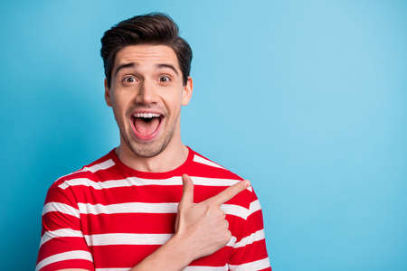 Photo of excited shocked young man point finger empty space discount news isolated on blue color backgroundの写真素材
