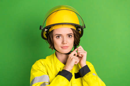 Photo of young woman firefighter serious confident tightening helmet uniform isolated over green color backgroundの写真素材
