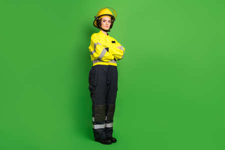 Full length photo of serious confident young firewoman dressed yellow uniform helmet arms crossed isolated green color backgroundの写真素材