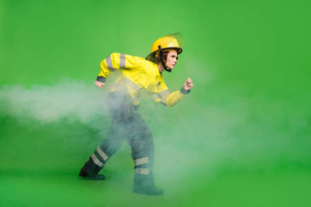 Full length photo of purposeful pretty young firewoman dressed uniform stalking through smoke isolated green color backgroundの写真素材