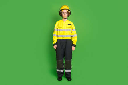 Full length photo of serious confident young firewoman dressed yellow uniform helmet isolated green...