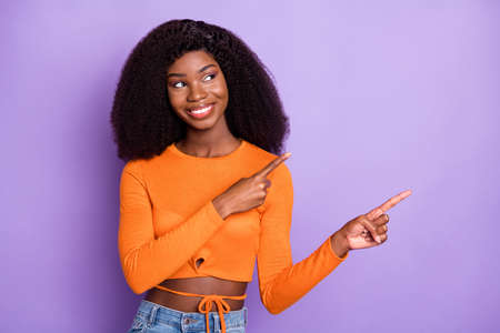 Photo of pretty cute dark skin woman dressed orange crop top looking pointing empty space isolated purple color backgroundの写真素材