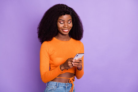 Portrait of lovely cheerful focused wavy-haired girl using device pastime blogging isolated over violet purple color backgroundの写真素材