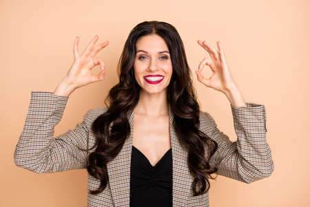 Photo portrait of girl showing two ok-signs isolated on pastel beige colored backgroundの写真素材