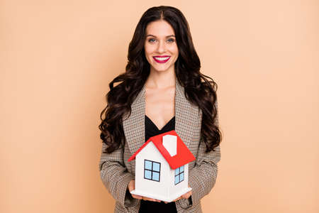 Photo portrait of girl holding small house model isolated on pastel beige colored backgroundの写真素材