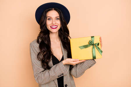 Photo of charming cute young woman wear plaid jacket headwear holding gift box isolated beige color...