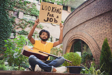 Photo portrait of jobless guy need money keeping carton table looking for work sitting on streetの写真素材