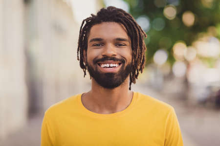 Photo portrait of young man in yellow t-shirt smiling wearing dreadlocks walking on city streetsの写真素材