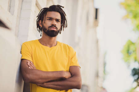 Photo portrait of confident serious man with dreadlocks standing on street with crossed hands...