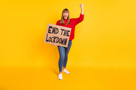Full size photo of blond hooray lady stand with poster wear red sweater jeans sneakers isolated on bright yellow color backgroundの写真素材