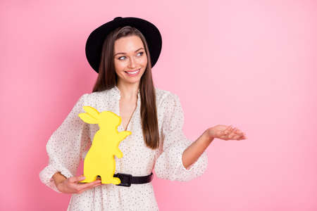 Photo of cool optimistic brunette lady hold paper rabbit look empty space wear headwear white shirt isolated on pastel pink color backgroundの写真素材