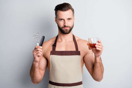 Portrait of attractive content fit guy wearing apron drinking beverage holding haircut tools isolated over light grey pastel color backgroundの写真素材
