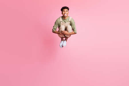 Photo of guy jump embrace knees beaming smile wear beige overall footwear isolated pink color...