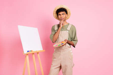 Photo portrait of african american painter thinking isolated on pastel pink colored backgroundの写真素材
