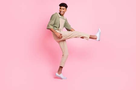Photo of handsome guy dance leg guitar playful look side wear beige overall sneakers isolated pink...