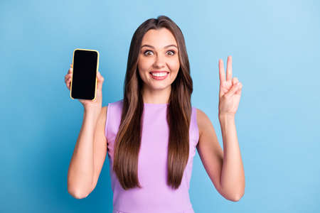 Photo portrait of young girl demonstrating mobile phone touchscreen copyspace showing v-sign...
