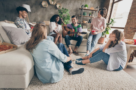 Portrait of attractive cheerful friends gathering playing guitar having fun pastime hobby holiday in house loft brick style interior indoorsの写真素材