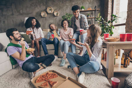 Portrait of attractive cheerful friends having fun eating junk snack communicating gathering in house loft brick style interior indoorsの写真素材