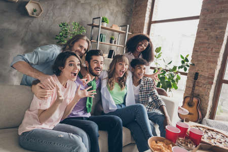 Portrait of attractive overjoyed cheerful friends gathering sitting on sofa having fun watching film in house brick loft style indoorsの写真素材