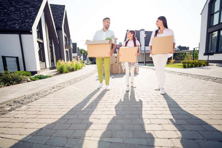 Full length body size view of three cheery family walking carrying packages cardboard belongings...