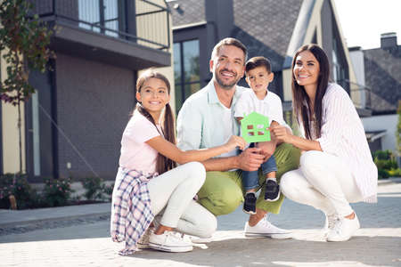 Full size photo of happy smiling positive family looking copyspace little boy hold small house paper...