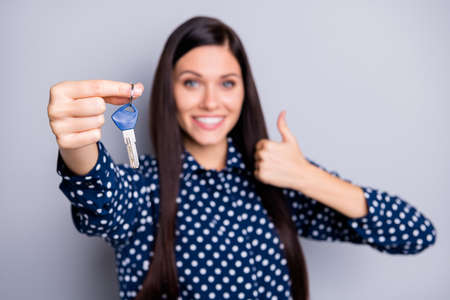 Photo of optimistic nice brunette girl show keys thumb up wear blue blouse isolated on grey color...