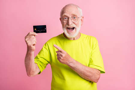 Photo of old positive cheerful excited grandfather wear lime t-shirt point finger at credit card isolated on pink color backgroundの写真素材