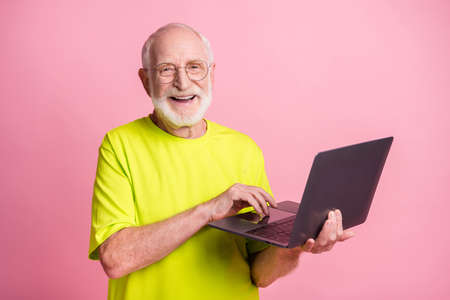 Portrait of funky pensioner typing laptop wear spectacles lime color t-shirt isolated on pastel pink...