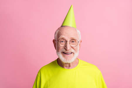 Portrait of optimistic pensioner wear birthday hat spectacles green color t-shirt isolated on pastel pink color backgroundの写真素材