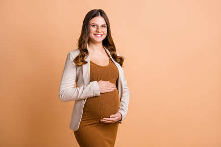 Photo of charming lady waiting baby dressed brown dress spectacles hugging tummy empty space isolated beige color backgroundの写真素材