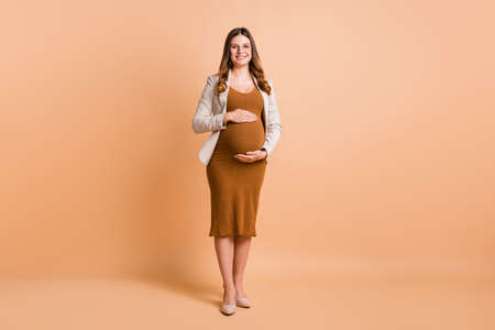 Photo of adorable charming woman expecting child wear jacket arms belly isolated beige color...