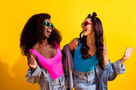 Photo of two shiny charming young ladies wear jeans outfit dark eyeglasses dancing looking each other isolated yellow color backgroundの写真素材