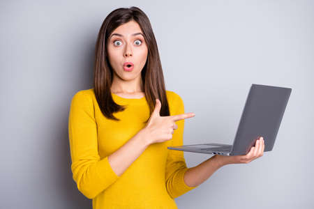 Photo of impressed brunette nice lady hold point laptop wear yellow sweater isolated on grey color backgroundの写真素材