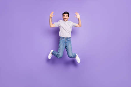 Photo of funny friendly guy jump raise two hands high five wear t-shirt denim jeans sneakers isolated violet backgroundの写真素材
