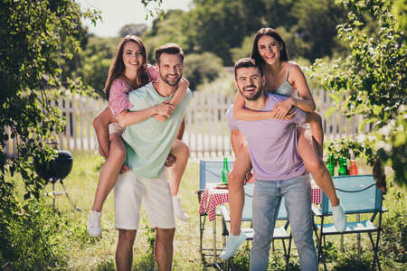 Photo of two couples company sitting piggyback having fun outdoors outside backyard forest...