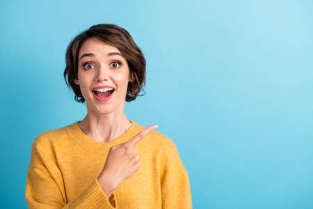 Photo portrait of surprised amazed female student wearing sweater showing blank space smiling isolated on vivid blue color backgroundの写真素材