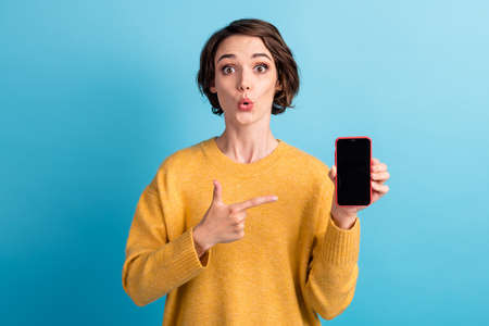 Photo of young shocked cool bob hairstyle lady point telephone wear yellow sweater isolated on blue color backgroundの写真素材