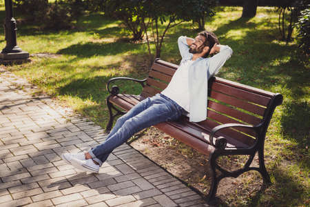 Full size profile side photo of charming relaxed afro american man sit bench rest hands above head outside in parkの写真素材