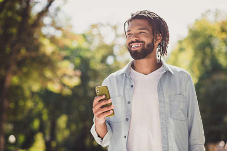 Portrait of attractive cheerful glad guy using device gadget strolling spending time on fresh air urban outside outdoorの写真素材