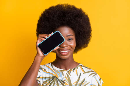 Portrait of nice cool curly hair lady showing telephone cover eye wear print t-shirt isolated over yellow color backgroundの写真素材