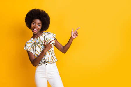 Photo of optimistic pretty curly hair lady point empty space wear print t-shirt isolated over yellow...